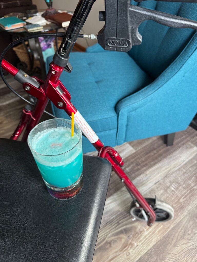A turquoise beverage with a straw sits on a black table next to a red NOVA scooter and blue armchair in an indoor setting.